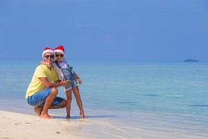 niña y padre feliz en sombrero de santa durante las vacaciones de navidad en la playa foto