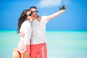 Happy couple taking a selfie photo on white beach. Two adults enjoying their vacation on tropical exotic beach