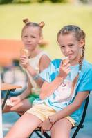 Little girls eating ice-cream outdoors at summer in outdoor cafe photo