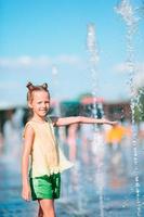 Little adorable girl have fun in street fountain at hot sunny day photo