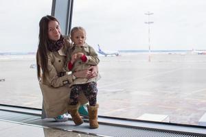 Mother and little daughter looking out the window at airport terminal photo