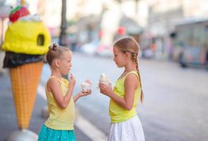 Happy little girls eating ice-creamin open-air cafe. People, children, friends and friendship concept photo