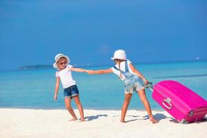 Little adorable girls with big suitcase on tropical white beach photo