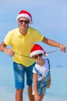 niña y papá feliz con sombrero de santa durante las vacaciones en la playa foto