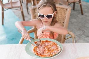 retrato de una linda niña sentada junto a la mesa y comiendo pizza foto