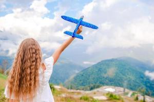 Happy little girl with toy airplane in hands in mountains photo