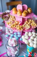 malvavisco, merengues de colores dulces, palomitas de maíz, pasteles de crema pastelera y pasteles blancos en la mesa festiva foto