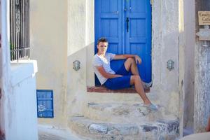 Young man sitting near old blue door of Emporio village on the island Santorini,Greece photo