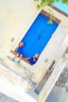 Two little adorable girls sitting on doorstep of old house in Emporio village, Santorini, Greece photo