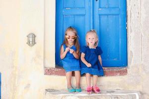 hermanitas lindas sentadas cerca de la antigua puerta azul en el pueblo griego de emporio, santorini foto