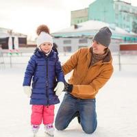 padre joven y adorable niña en una pista de patinaje foto