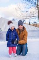 padre joven y adorable niña en una pista de patinaje foto