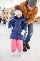 joven padre enseñando a su pequeña hija a patinar en la pista foto