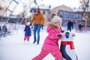 retrato de una niña adorable patinando en el fondo de la pista de hielo, su padre y su hermana pequeña foto