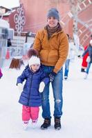 joven padre feliz y adorable niña en una pista de patinaje foto