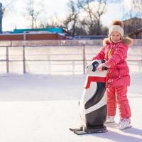 Little cheerful girl learning to skate on the rink photo