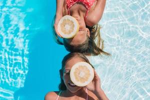 Little girls covering eyes with lemon halves near eyes on background swimming pool photo