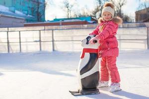 Little cheerful girl learning to skate on the rink photo
