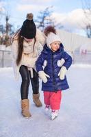 feliz adorable niña y joven madre aprendiendo patinaje sobre hielo foto