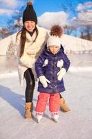 feliz adorable niña y joven madre aprendiendo patinaje sobre hielo foto