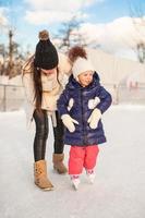 Young mother teaching her little daughter to skate on ice-rink photo