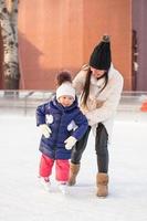 feliz adorable niña y joven madre aprendiendo patinaje sobre hielo foto