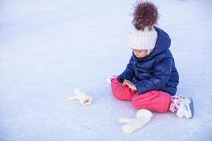 Little adorable girl sitting on ice with skates after the fall photo