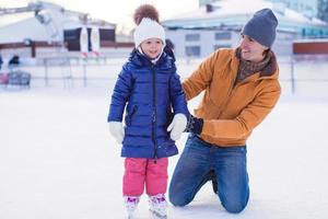 joven padre feliz y adorable niña en una pista de patinaje foto