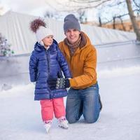 Young happy father and adorable little girl on a skating rink photo