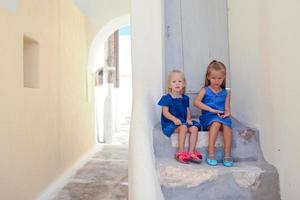 Two little adorable girls sitting on doorstep of old house in Emporio village, Santorini, Greece photo