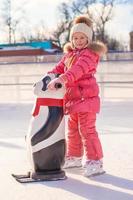 Little happy girl learning to skate on the rink photo