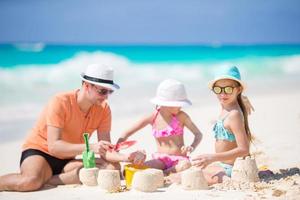 padre e hijas pequeñas haciendo castillos de arena en la playa tropical foto