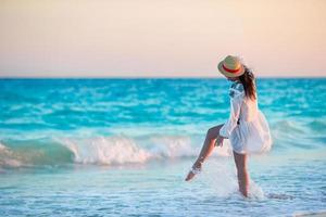 Young beautiful woman on tropical beach in sunset. Back view of young girl in beautiful dress background the sea photo