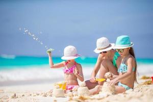 madre e hijas pequeñas haciendo castillos de arena en la playa tropical