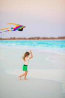 Little girl with flying kite on tropical beach. Kid play on ocean shore. Child with beach toys. photo