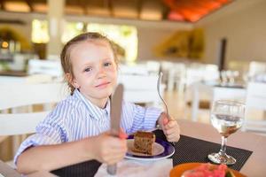 Adorable little girl having breakfast at outdoor cafe photo