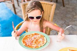 Little girl eating pizza on dinner time photo