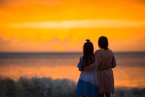 Adorable happy little girls walking on white beach at sunset. photo