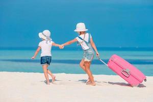 Little tourists girls with big suitcase on tropical white beach photo