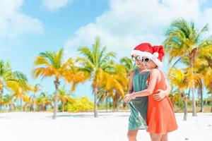Little adorable girls in Santa hats during beach vacation have fun together photo