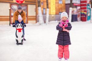 adorable niña en la pista de patinaje con padre y linda hermana en el fondo foto