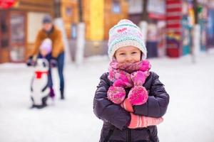 adorable niña en la pista de patinaje con padre y hermana en el fondo foto