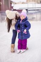 feliz adorable niña y joven madre aprendiendo patinaje sobre hielo foto