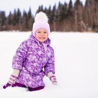 Little happy adorable girl sitting on the snow at winter sunny day photo