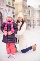 feliz adorable niña y joven madre patinando sobre hielo foto