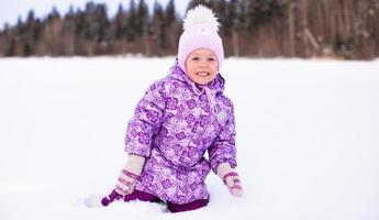 Little happy adorable girl having fun on the snow at winter sunny day photo