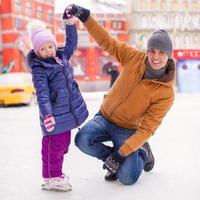 niña feliz con padre joven divertirse en la pista de patinaje foto