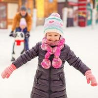 adorable niña en pista de patinaje con padre y hermana foto