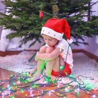 Little beautiful girl in Santa Claus hat sitting under the Christmas tree among garlands photo