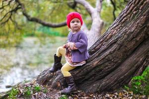 Cute little girl in a red cap near lake at the autumn park photo